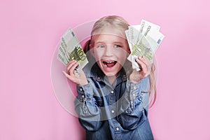 Business and money concept - happy little girl with euro cash money over pink background