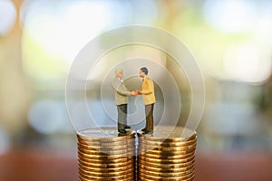 Business Money and Finance Concept, Two businessman miniature figure people standing and make a hand shake on top of stack of gold