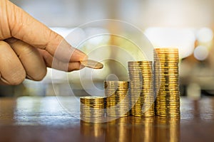 Business, Money, Finance and Saving Concept. Close up of man hand holding and put a coin to stack of coins on wooden table