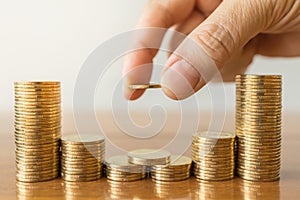 Business, Money, Finance, Secure and Saving Concept. Close up of man hand holding and put a coin to stack of coins on wooden table