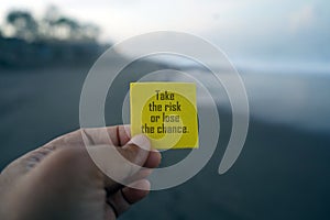 Business motivational inspirational quote - Take the risk or lose the chance. With person holding yellow card in hand.