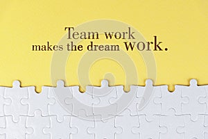 Business motivational quote - Team work makes the dream work. On yellow background of white jig saw puzzle missing pieces.