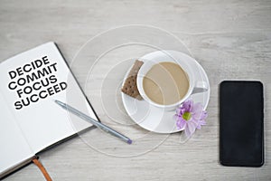 Business motivational words - Decide commit focus succeed. Written on open book with pen, cup of coffee with purple flower