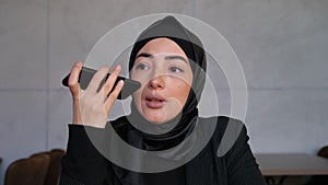 Business Muslim woman in hijab leaves a voice message on the mobile phone. Concept of technology, assistant help