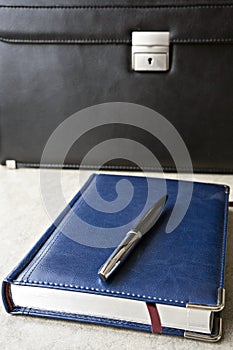 Business notebook and pen  on the table in front of the briefcase