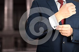 Business and office concept - elegant young fashion buisness man in a blue/navy suit touching at his cufflinks photo