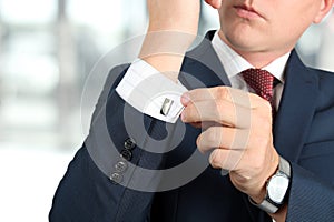 Business and office concept - elegant young fashion buisness man in a blue/navy suit touching at his cufflinks photo