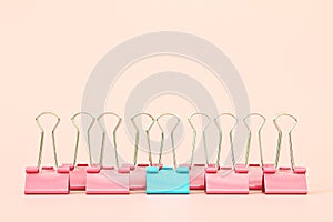 Blue binder clip standing out of pink binder clips on pink background with copy space