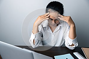 A business office worker is an asian woman is sitting in front of the laptop computer. A businesswoman stressing her body part