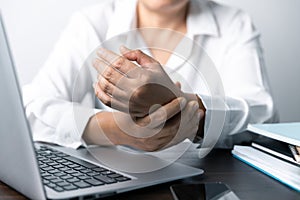 A business office worker is an asian woman is sitting in front of the laptop computer. A businesswoman stressing her body part