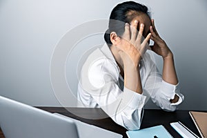 A business office worker is an asian woman is sitting in front of the laptop computer. A businesswoman stressing her body part