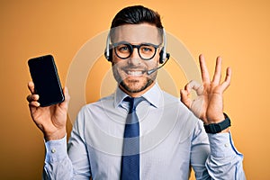 Business operator man with customer service headset from call center showing smartphone screen doing ok sign with fingers,