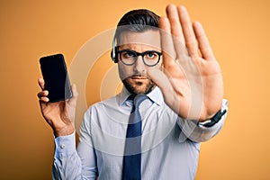 Business operator man with customer service headset from call center showing smartphone screen with open hand doing stop sign with