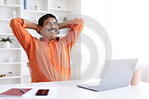 Cheerful dreamy mature indian man sitting at home office