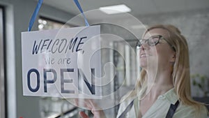 Business owner an attractive woman in an apron and glasses changes the sign on the front door from CLOSED to OPEN