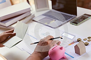 Business owner checking saving account passbook and using a calculator with money coin, piggy bank, laptop, budget and income