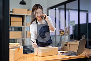 Business owner talking on mobile phone and taking order. Female asian entrepreneur working at home office confirming the