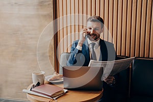 Business owner talking on phone after reading news, sitting in cafe