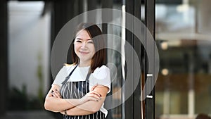 A business owner woman standing with arms crossed and smiling to camera at her coffee shop.