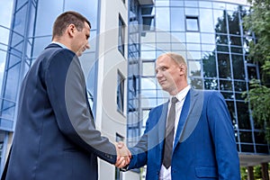 Business partners handshaking near office building outdoors