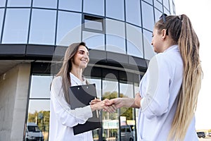 Business partners handshaking before office building. Two beautiful women in business suits smiling each other