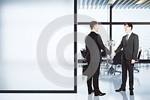 Business partners shake hands in modern conference room with blank white wall, mock up