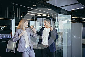 business people celebrating a successful deal, dancing in the office, Asian man and blonde woman