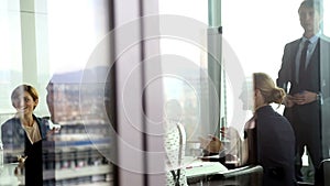 Business people clapping to colleague in conference room, behind glass wall