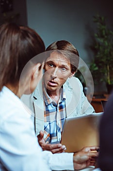 Business people communicating sitting at workplace in office. Selective focus on serious Caucasian man. Toned image