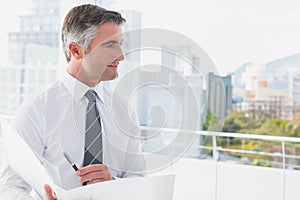 Mature man standing on office balcony reviewing documents while holding folder and pen, copy space