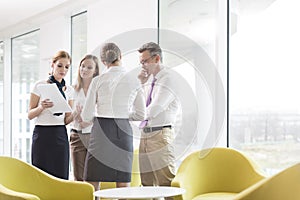 Business people discussing over documents in office lobby