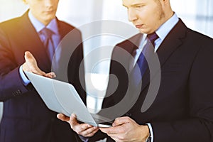 Business people discussing a presentation at meeting, standing in a sunny modern office. Unknown businessman with a