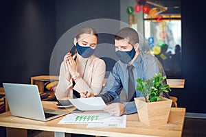 Business people with face masks working together on laptop in modern coworking office