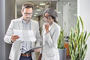 Business people in formal wear reading document in office hall.