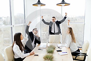 Business people in formalwear celebrate victory while sitting together at the table