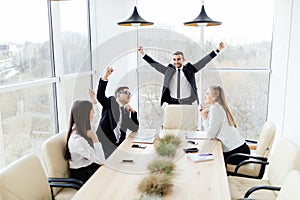 Business people in formalwear celebrate victory while sitting together at the table