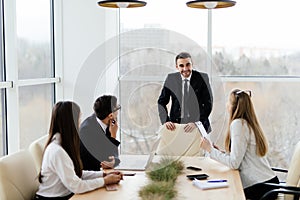 Business people in formalwear discussing with leader something while sitting together at the table