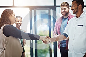 Business people giving handshake, welcoming new employee and standing united while colleagues clap in meeting at work