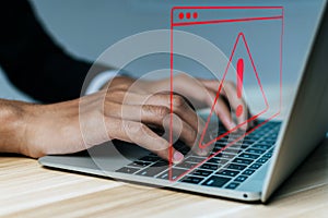 Business people hand using laptop computer with virtual malware attack warning graphic icon on desk