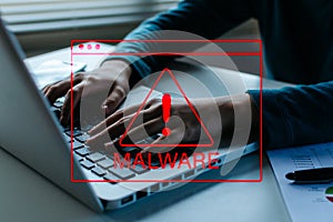 Business people hand using laptop computer with virtual malware attack warning graphic icon on desk