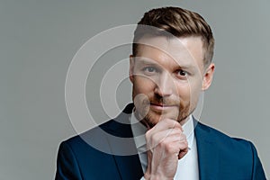 Handsome thoughtful entrepreneur thinking about business and looking at camera while standing against grey background