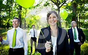 Business people holding green balloon in forest.