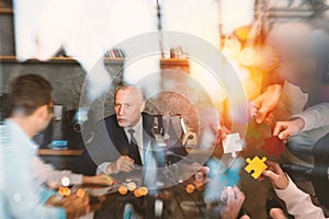 Business people join puzzle pieces in office. Concept of teamwork and partnership. double exposure with light effects