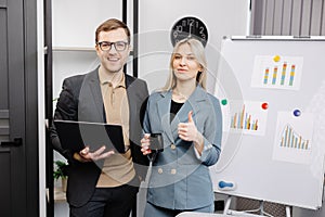 Business people with laptop discussing new projects in office. A young woman and a man stand near flipcharts and solve work issues