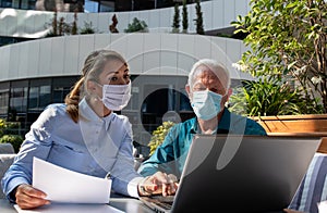 Business people with maska working on laptop outdoor