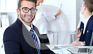 Business people at meeting in office. Focus at cheerful smiling bearded man wearing glasses. Conference, corporate