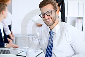 Business people at meeting in office. Focus at cheerful smiling bearded man wearing glasses. Conference, corporate