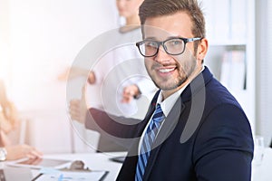 Business people at meeting in office. Focus at cheerful smiling bearded man wearing glasses. Conference, corporate