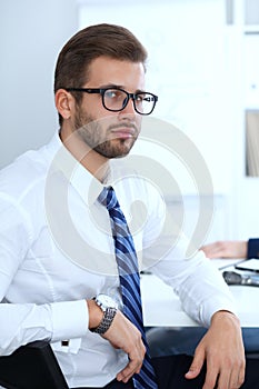 Business people at meeting in office. Focus at cheerful smiling bearded man wearing glasses. Conference, corporate