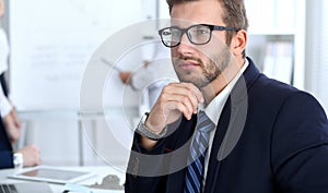 Business people at meeting in office. Focus at cheerful smiling bearded man wearing glasses. Conference, corporate